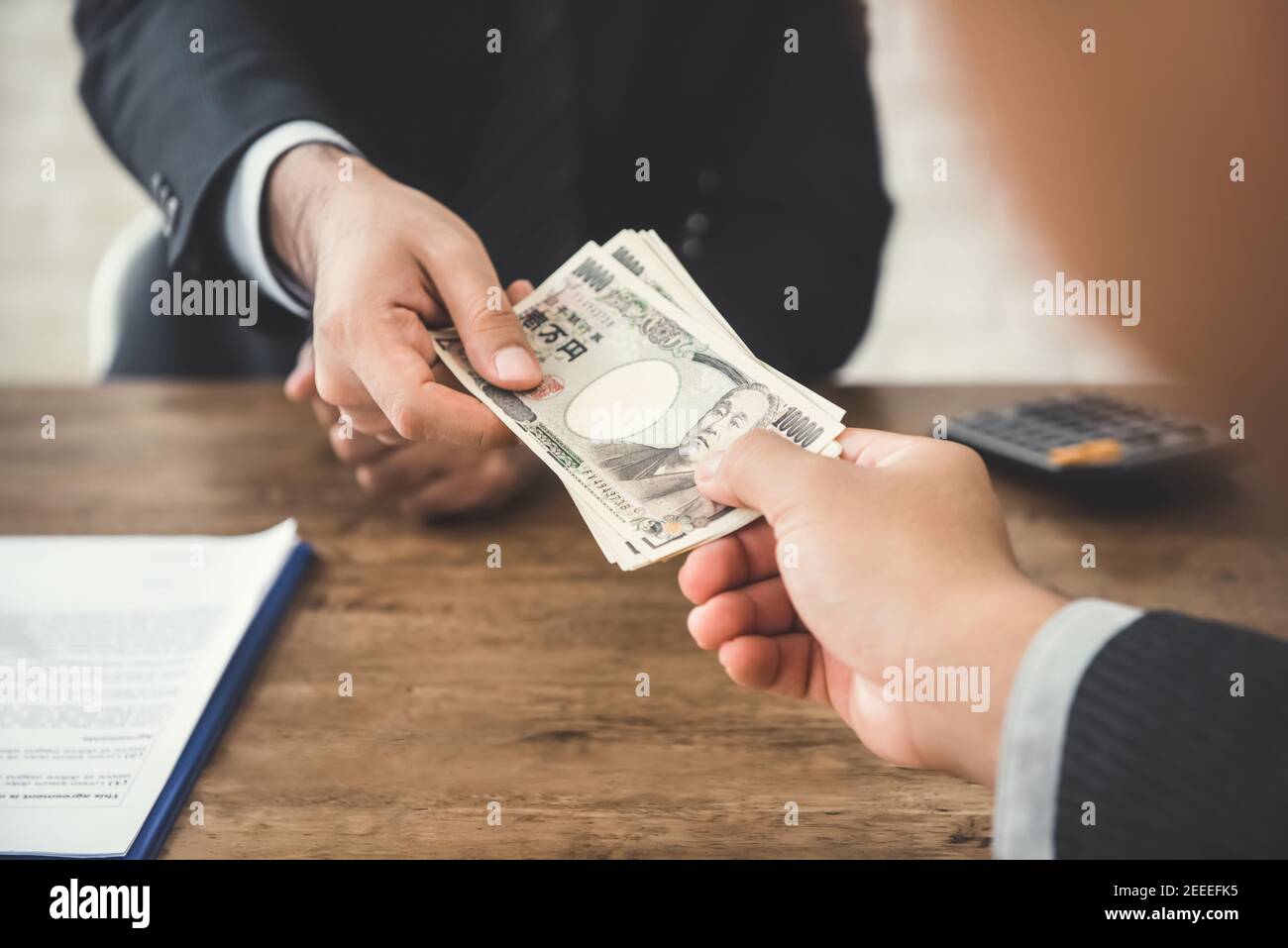 Businessman giving money, Japanese yen currency, to his partner at the table Stock Photo