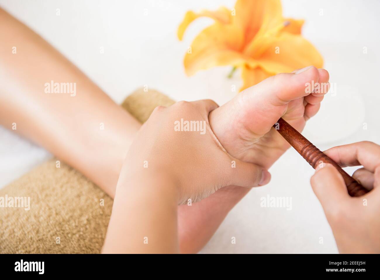 Professional therapist giving relaxing reflexology Thai foot massage with stick to a woman in spa Stock Photo