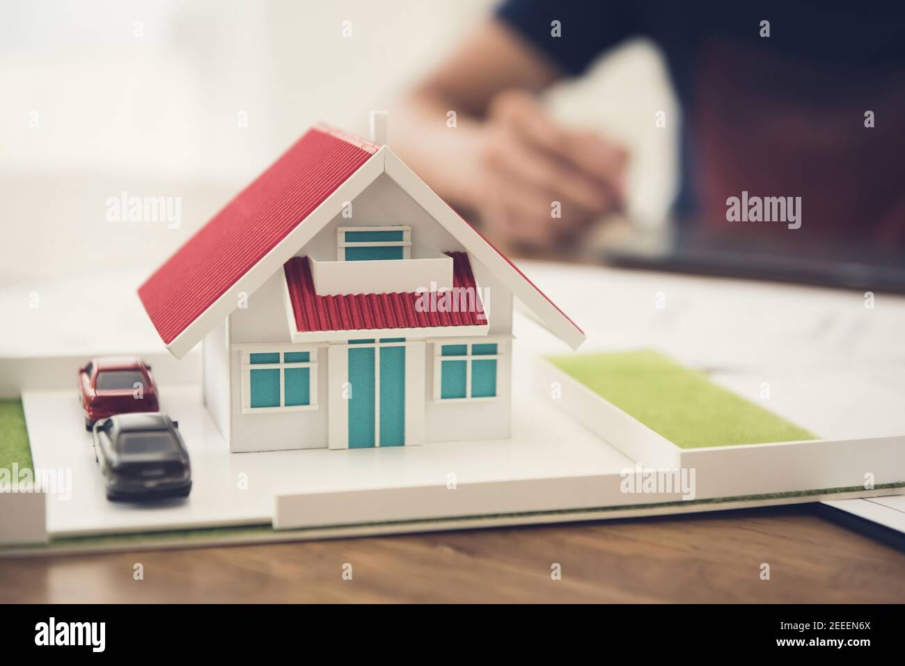 Car and house model on the table with blur working people in background - architecture and real estate service concept Stock Photo