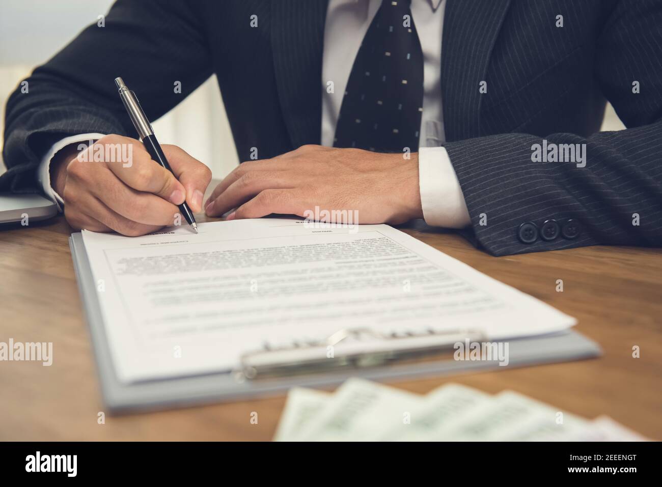 Businessman signing legal business contract agreement with money on the table Stock Photo