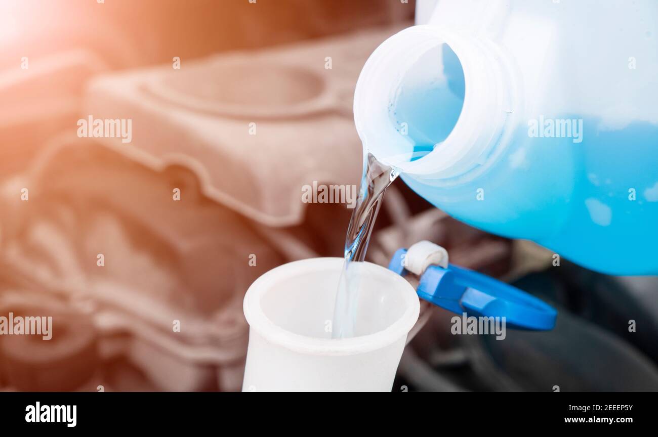 Pouring liquid from plastic canister into car washer fluid reservoir