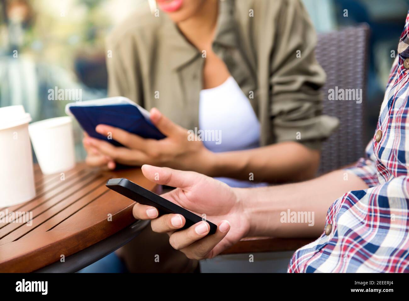 People concentrating on using smartphone and tablet computer while sitting in coffee shop - social media addiction concept Stock Photo