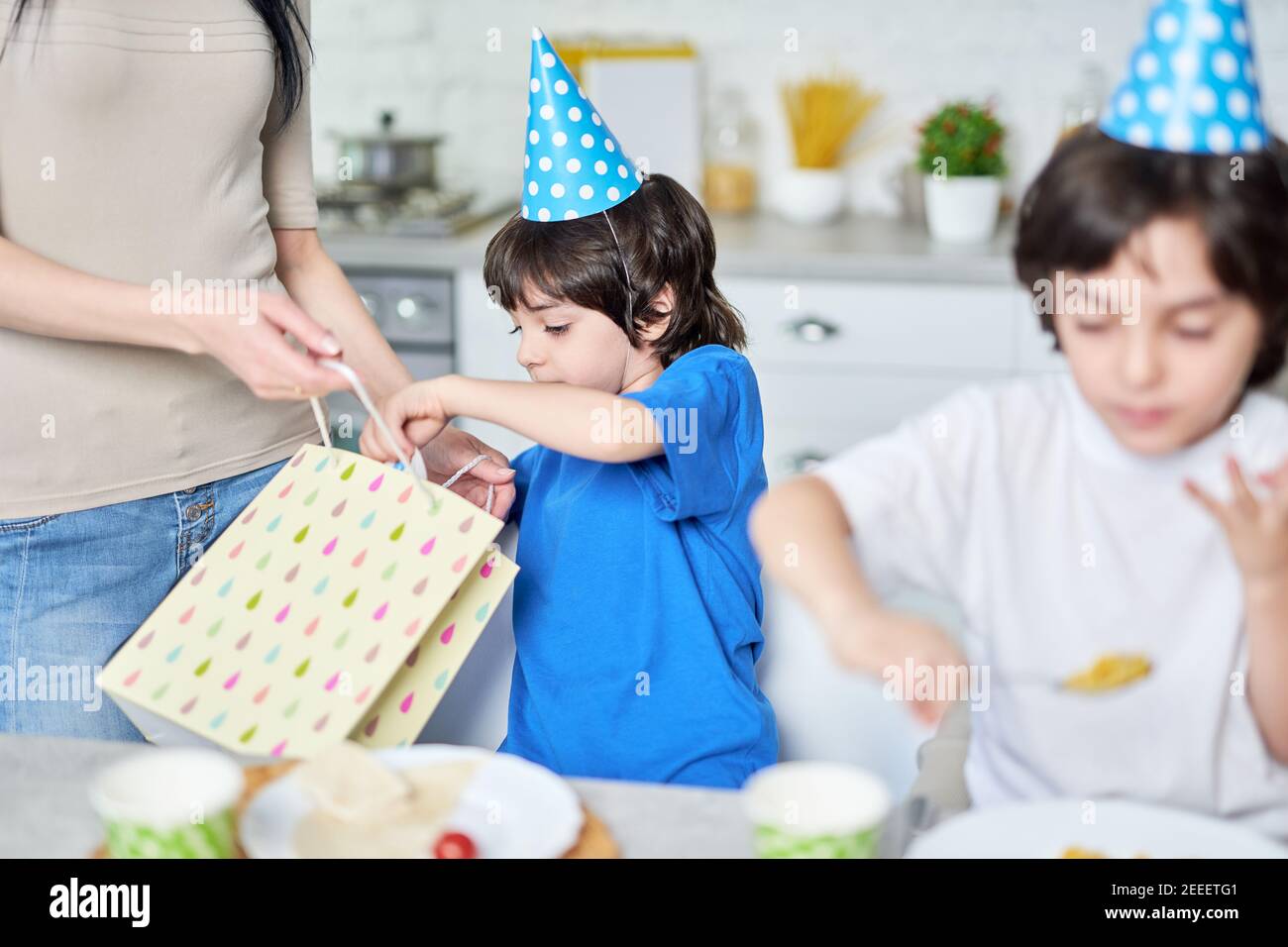 Cute little boy in birthday cap receiving presents fron his parents. Latin family celebrating birthday together at home. Childhood, celebration concept. Selective focus Stock Photo
