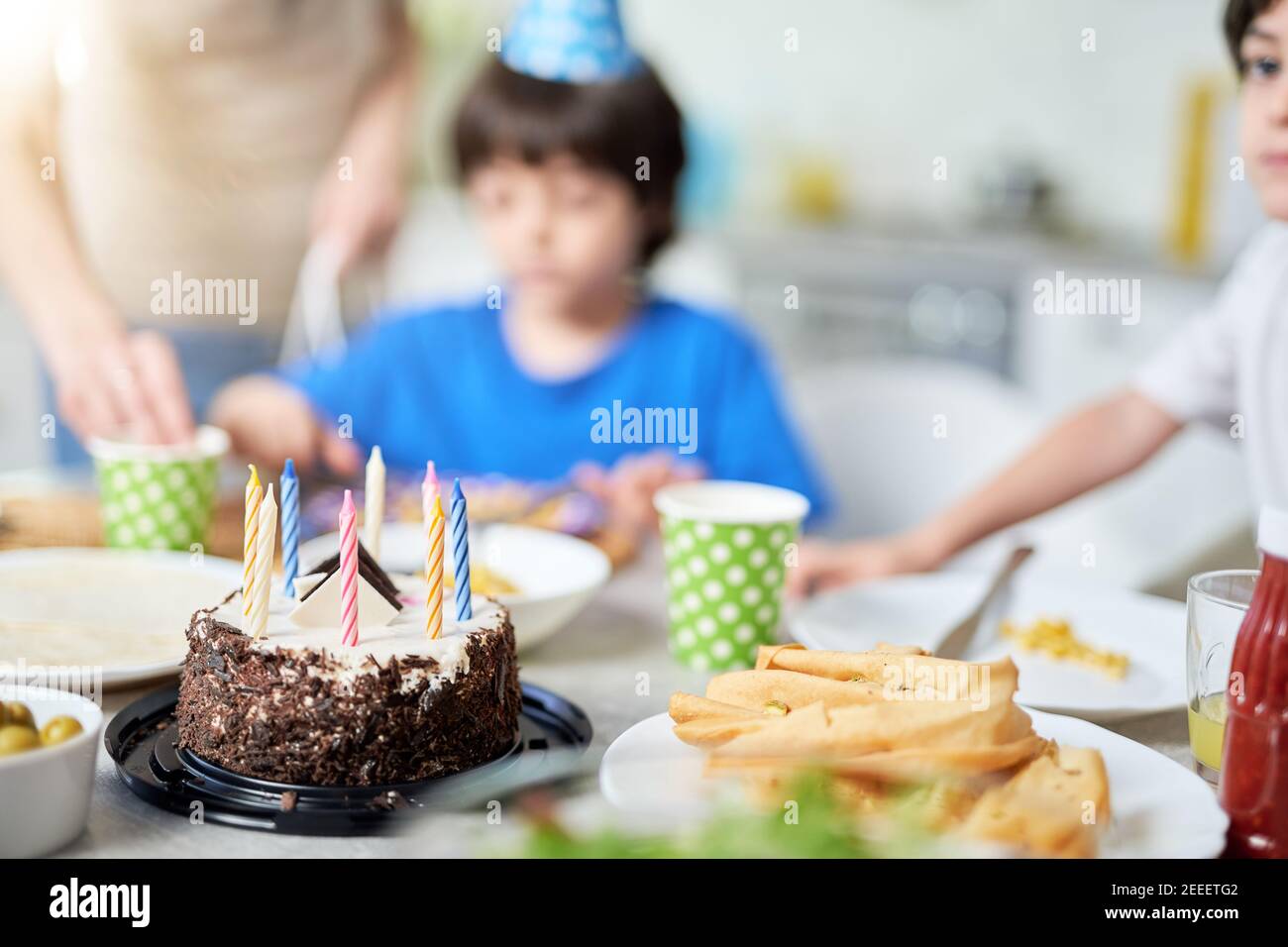 Close up of a birtday cake with candles on the table. Happy hispanic family with kids celebrating birthday at home. Selective focus Stock Photo