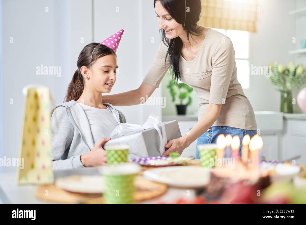 Happy latin mother gives gift box to her lovely daughter, greeting her while celebrating child birthday at home. Selective focus. Family, celebration concept Stock Photo