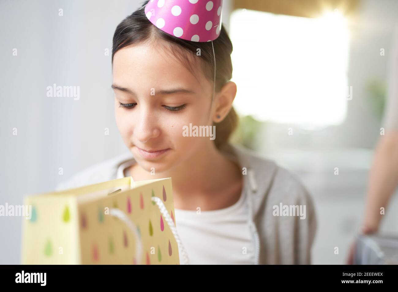Curious teenaged hispanic girl checking, looking inside gift bag, while receiving presents, celebrating birthday at home. Celebration, childhood concept Stock Photo
