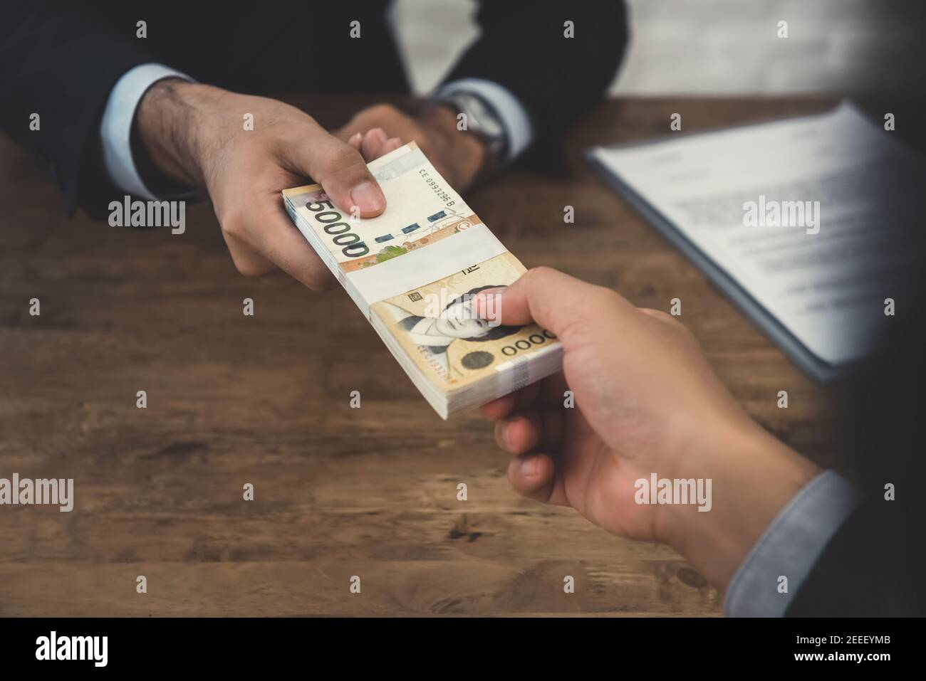 Businessman giving money, South Korean won banknotes, to his partner at the desk Stock Photo