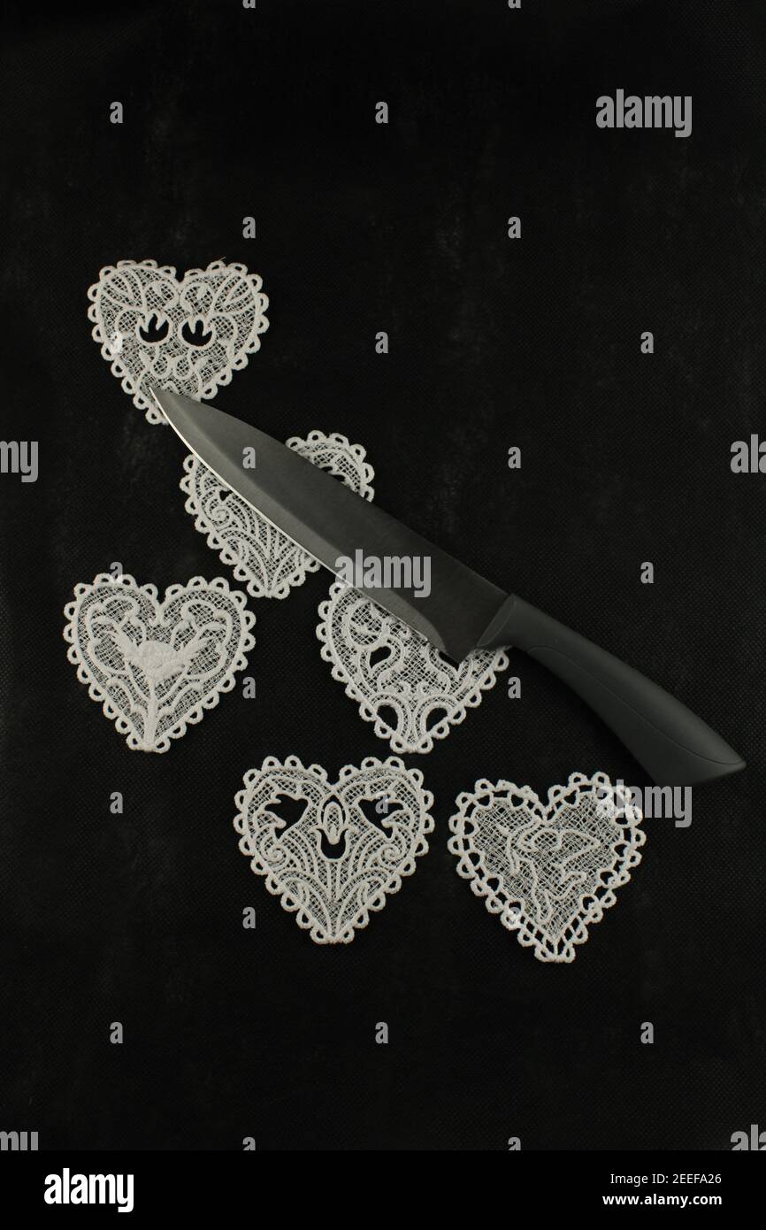 Knife laying across six lace hearts on a black background, breakdown of relationship concept Stock Photo
