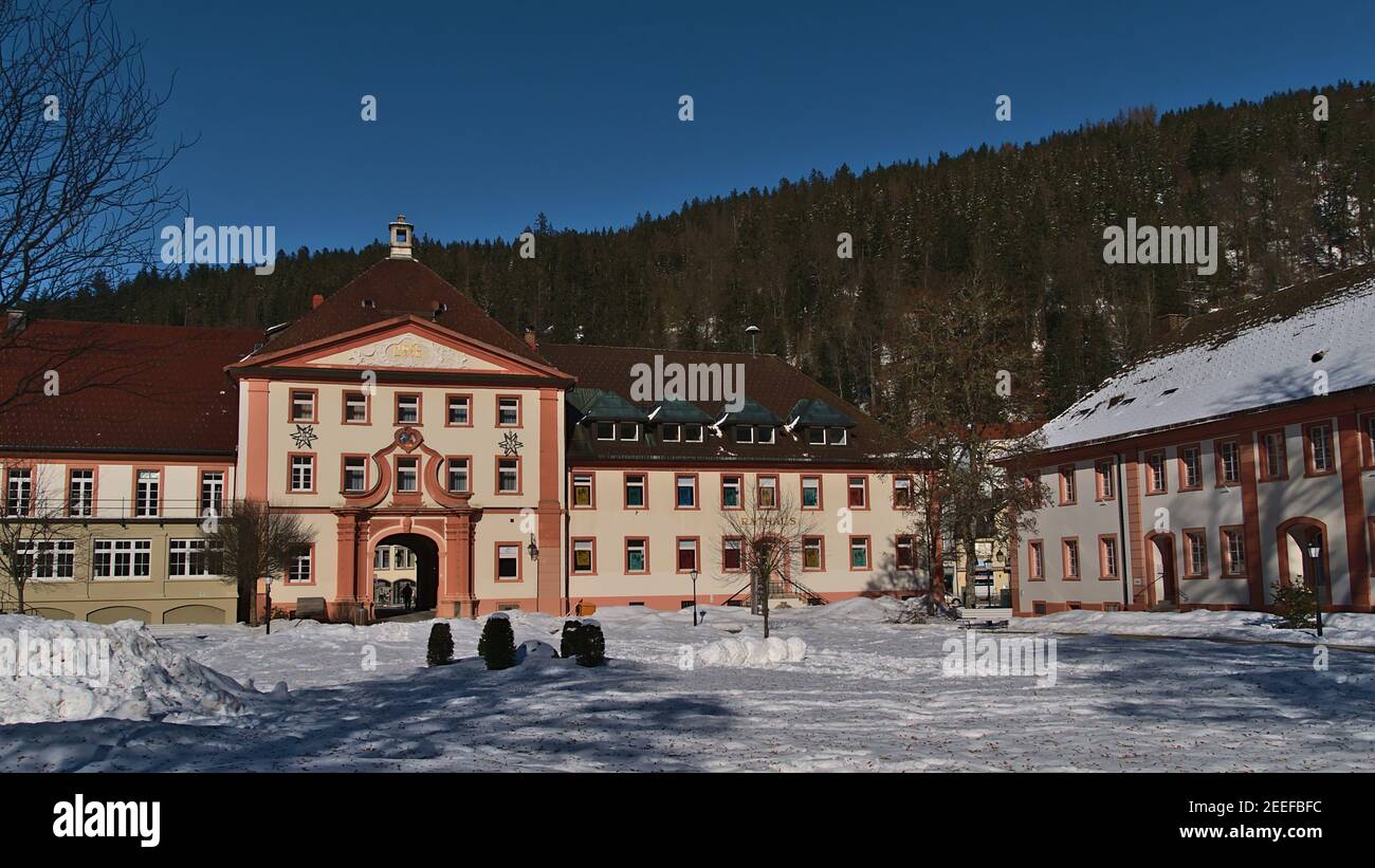 View of town hall (left) and catholic rectory (right) located in old buildings in town center in winter season with snow-covered square on sunny day. Stock Photo