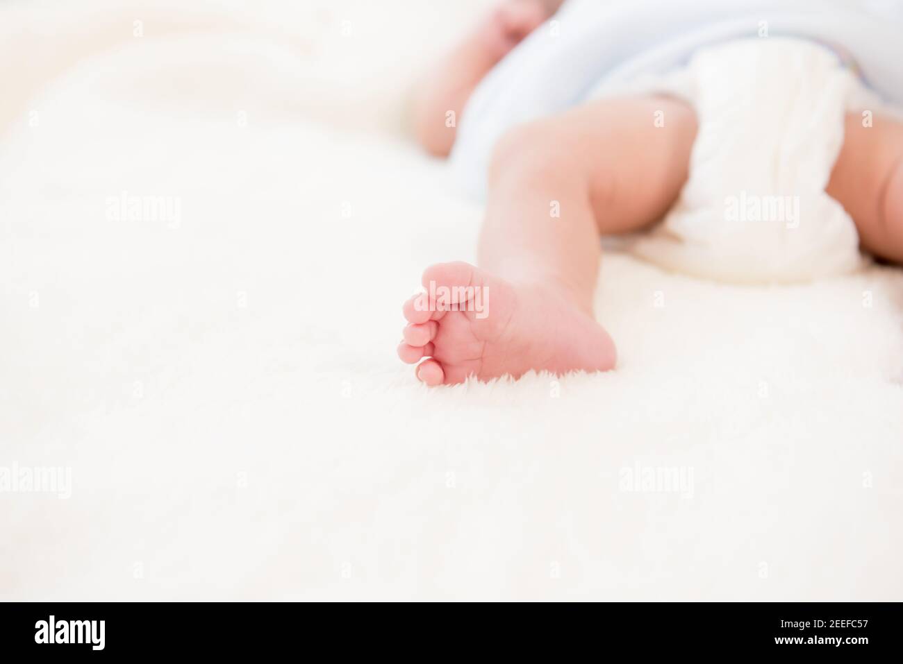Small little foot of newborn baby on soft white wool fluff sheet Stock Photo