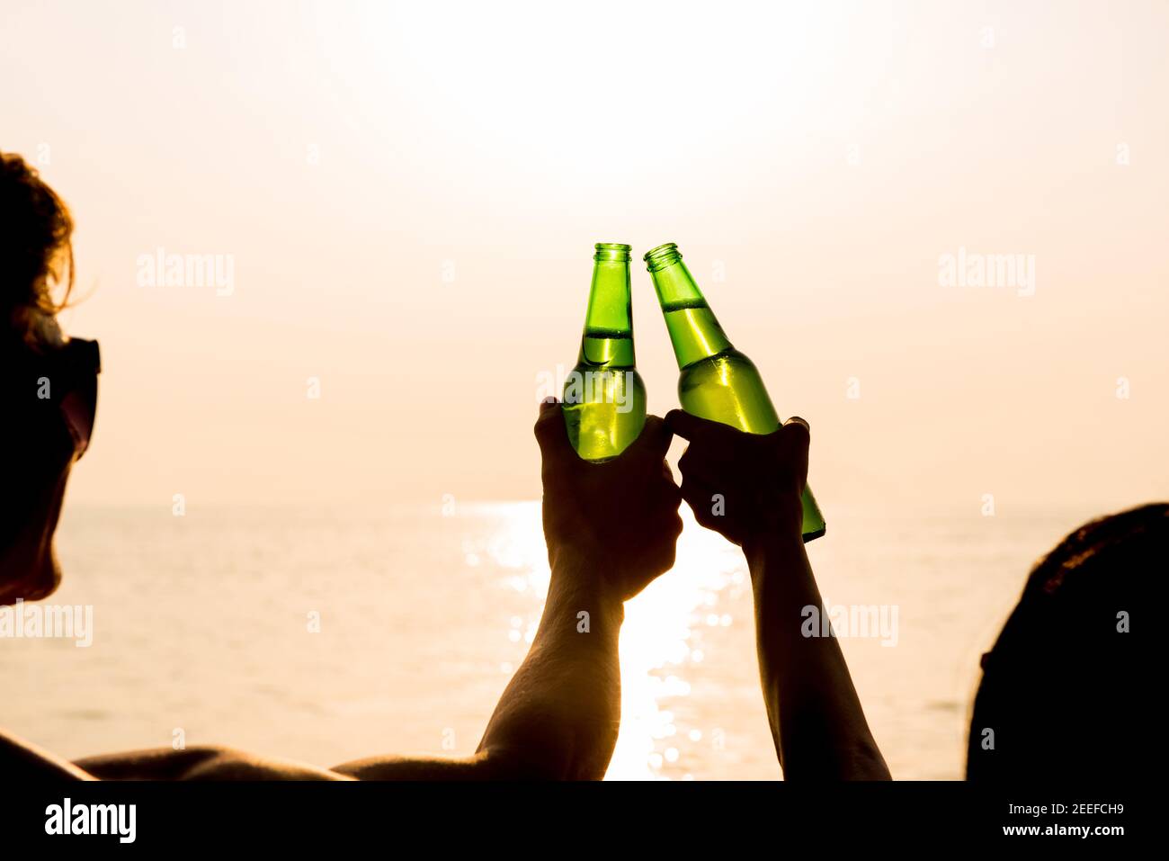 Couple clanging bottles of beers, celebrating on holiday at the beach in summer sunset Stock Photo