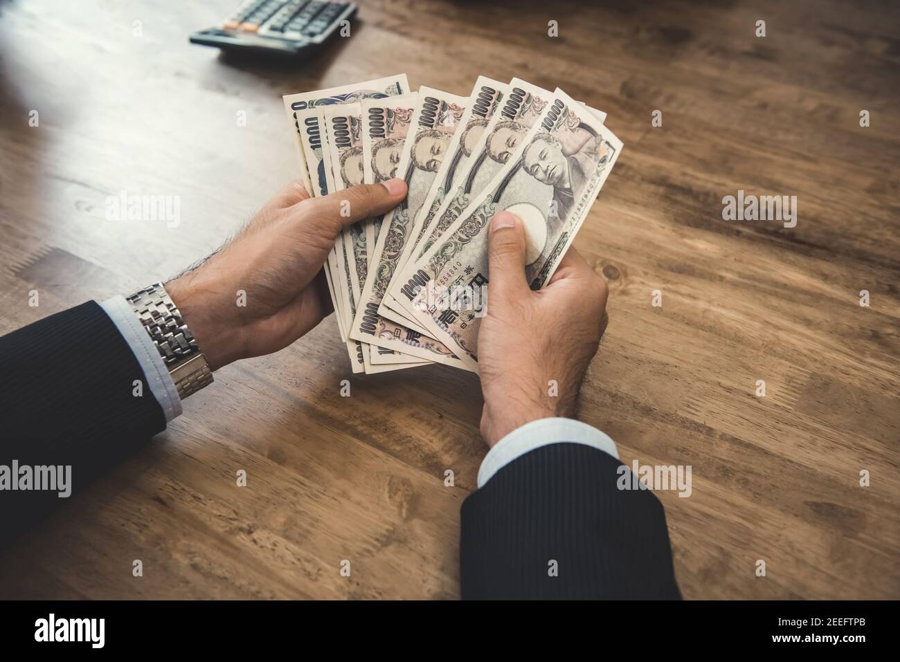 Businessman counting money, Japanese yen banknotes, at wooden table Stock Photo