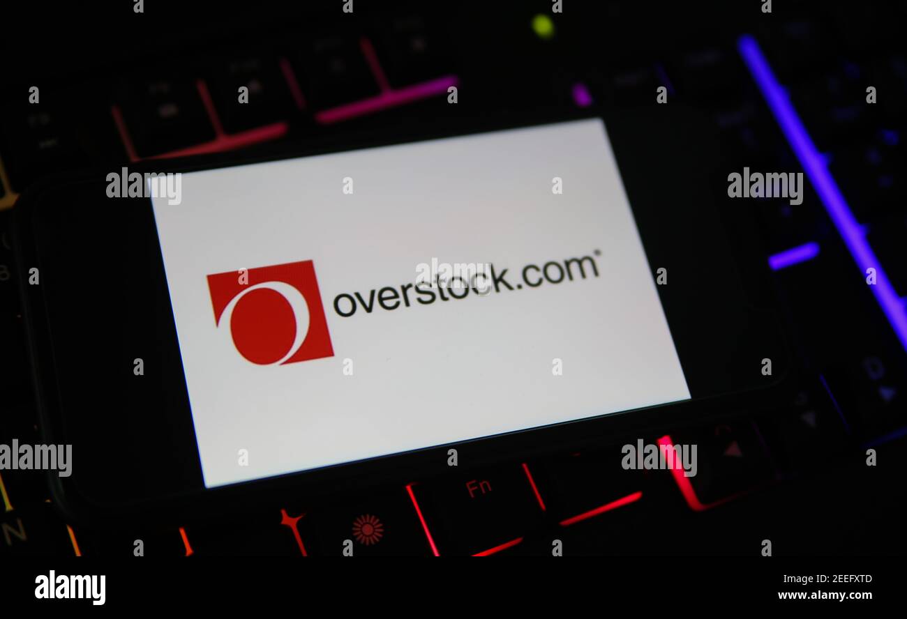 Viersen, Germany - February 9. 2021: Closeup of smartphone screen with logo lettering of overstock.com on blurred computer keyboard Stock Photo
