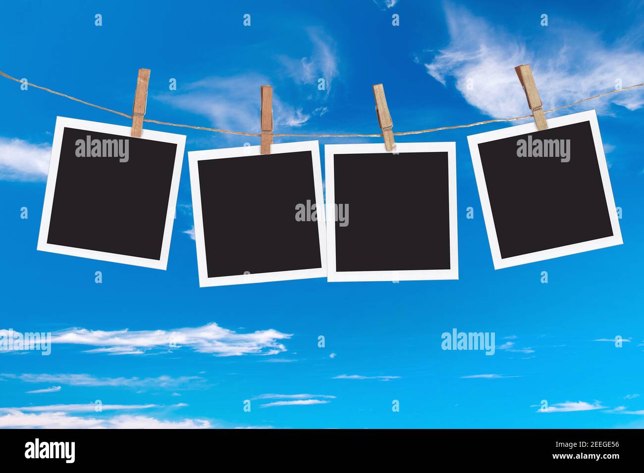 Four blank instant photo frames hanging on a rope, on blue sky background Stock Photo