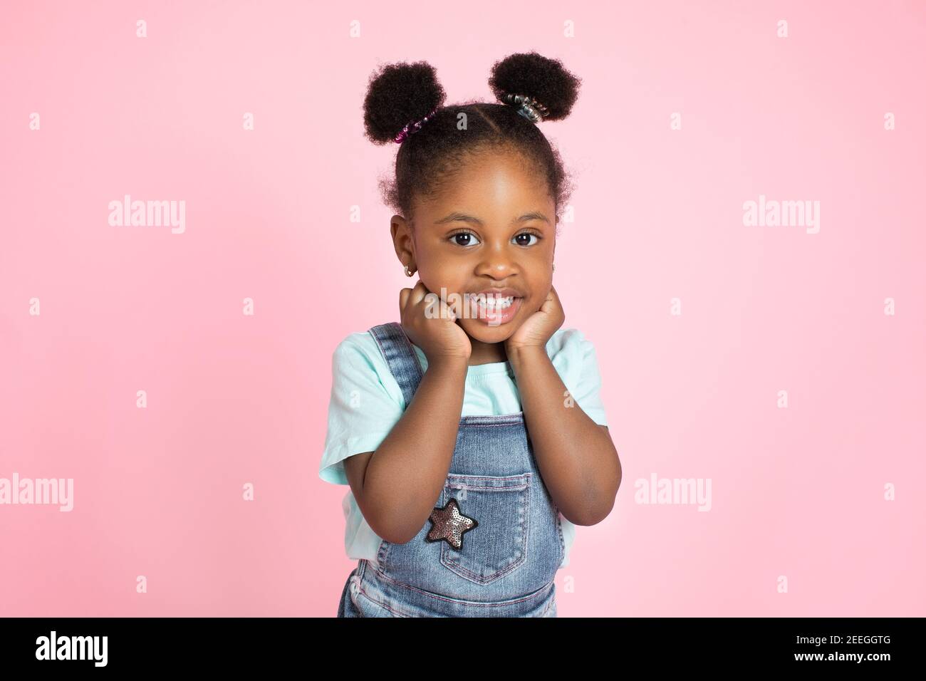Funny happy smiling little cute African-american girl, with afro hair in  two ponytails, posing with her arms under face and looking at camera over  Stock Photo - Alamy