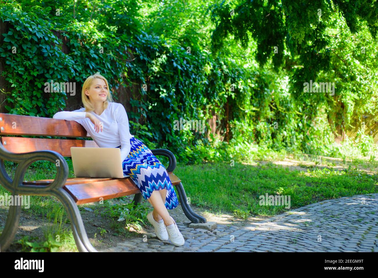 Shopping online. Girl sit bench with notebook. Woman with laptop in park enjoy green nature and fresh air. Girl dreamy takes advantage of online shopping. Save your time with shopping online. Stock Photo
