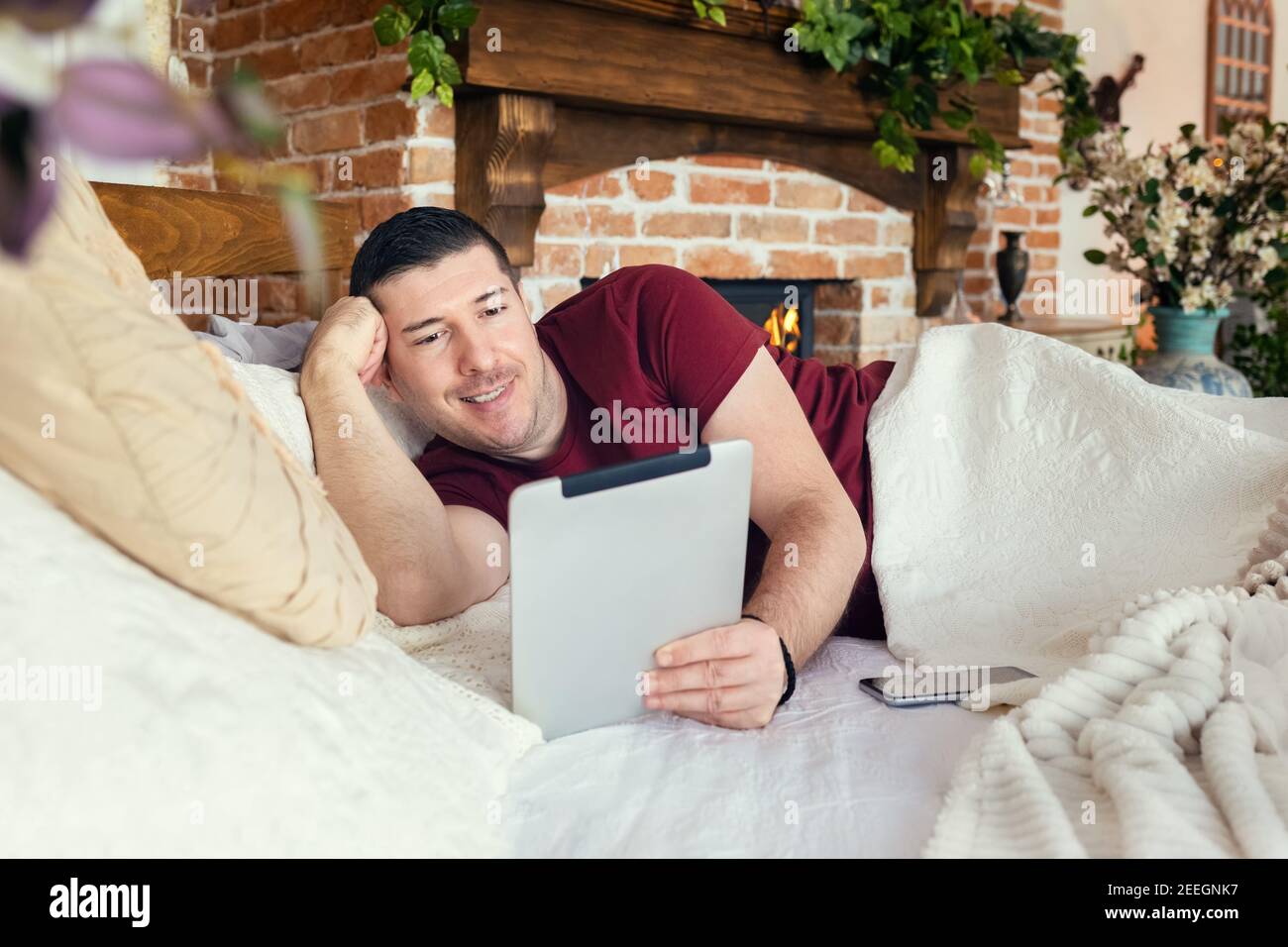 Happy man chatting on digital tablet app while relaxing in cozy bed at home Stock Photo