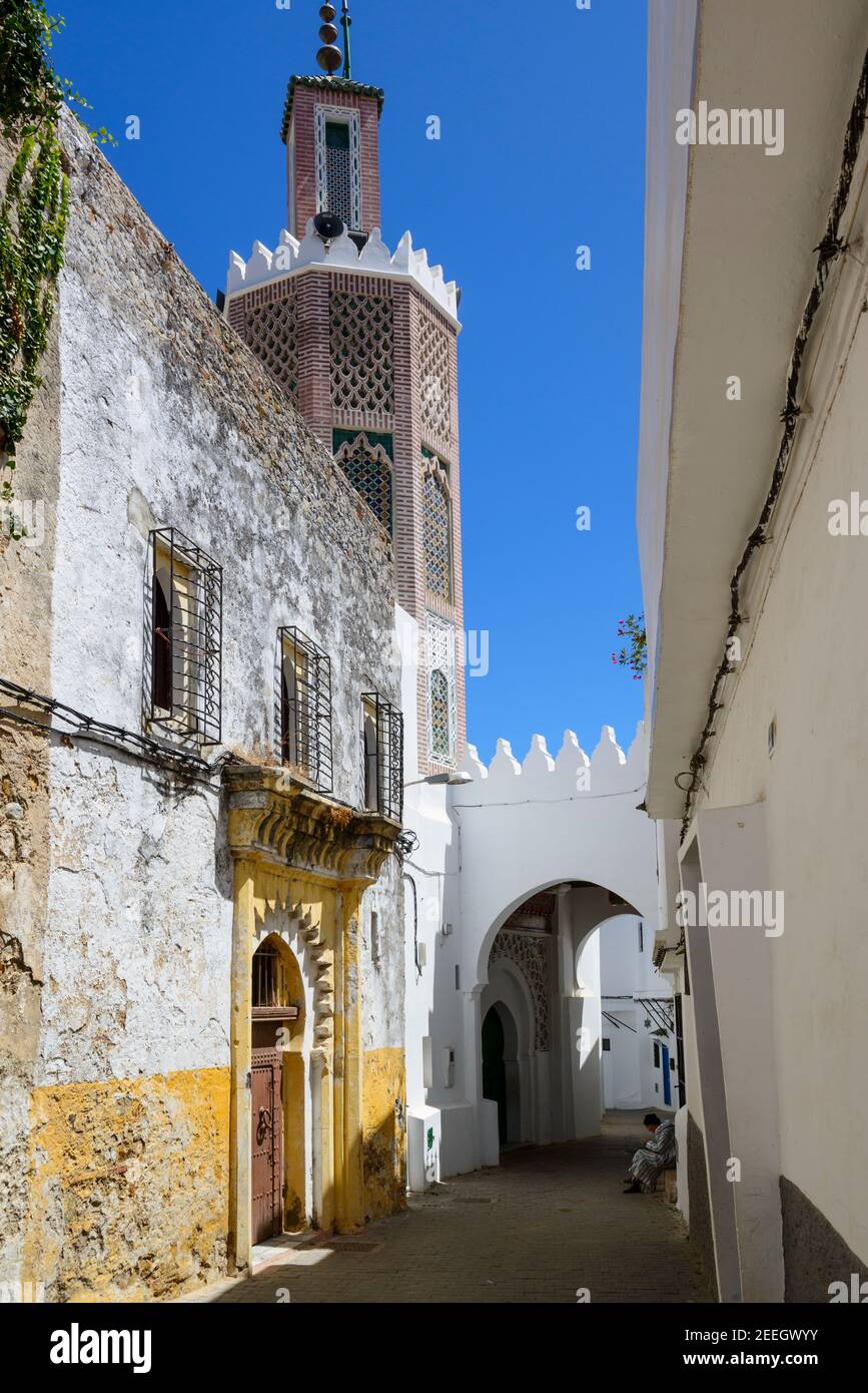 A man wearing a striped djellaba sits in front of a small mosque on the threshold of a house in the medina of Tangier, Morocco. Stock Photo