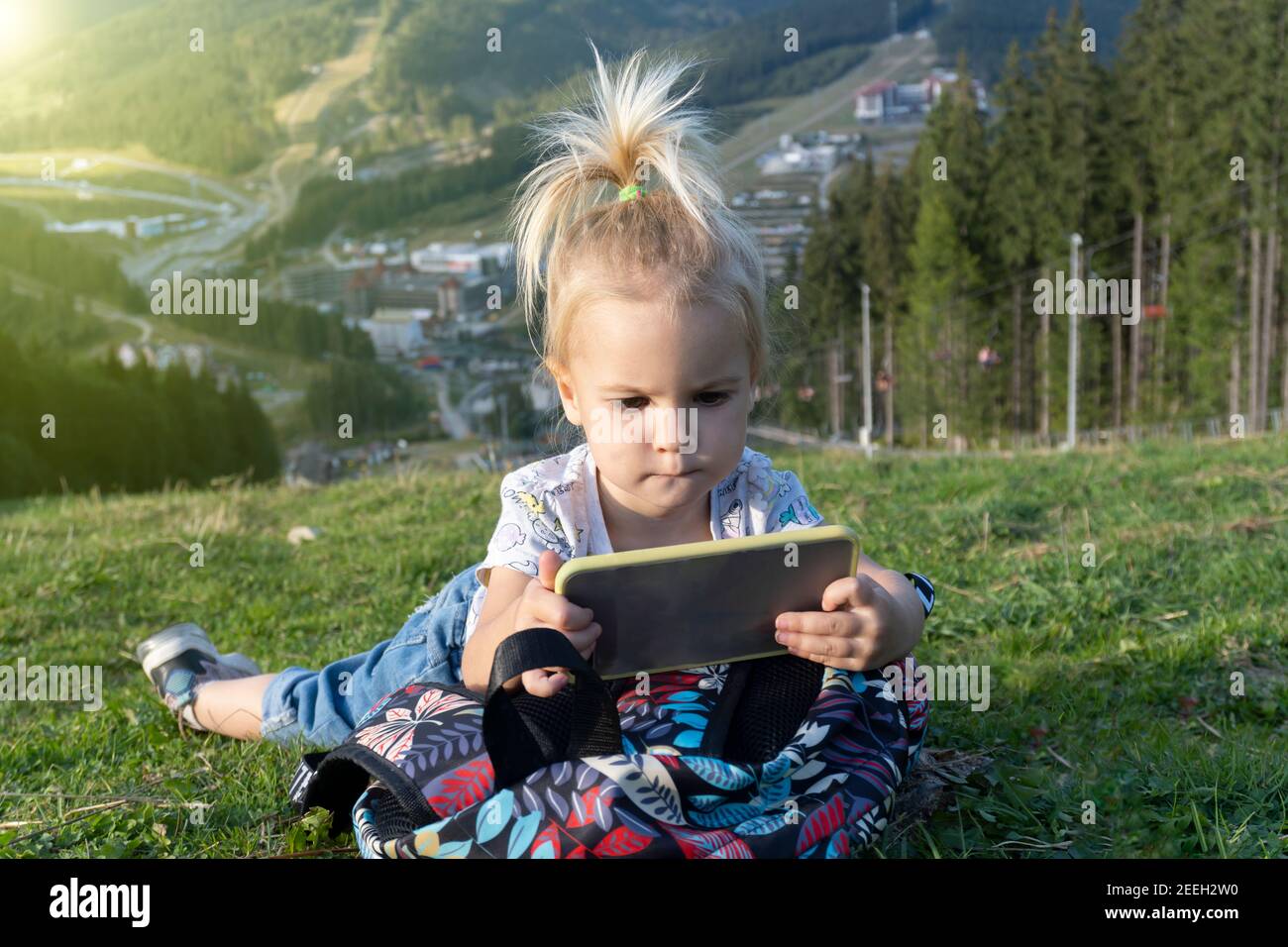 Child laying at green grass and looking at mobile phone with interested face Stock Photo