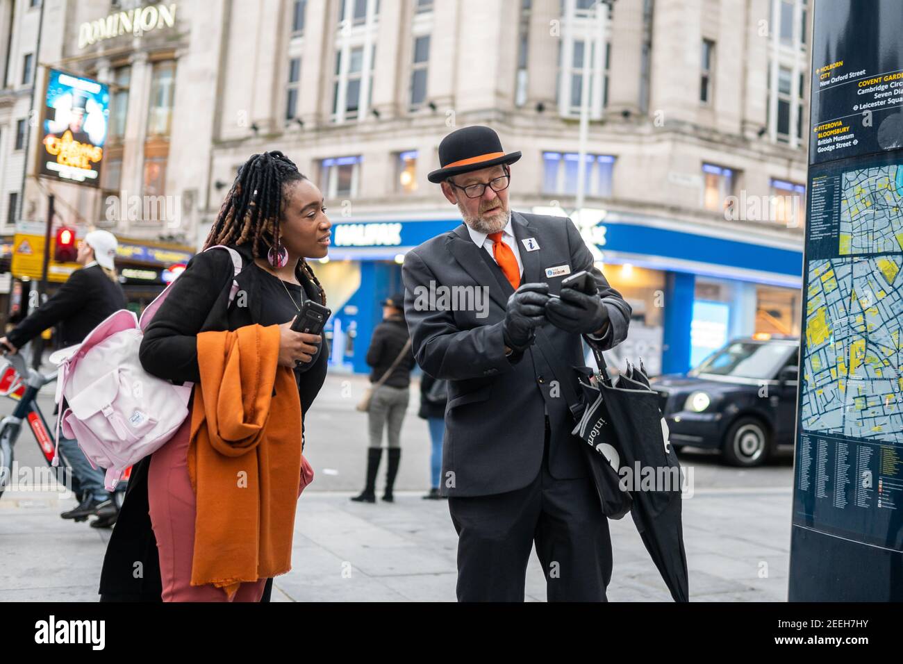 London Westminster Tourist information guide traditional suit bowler hat orange tie umbrella giving directions to woman in the shopping high street Stock Photo