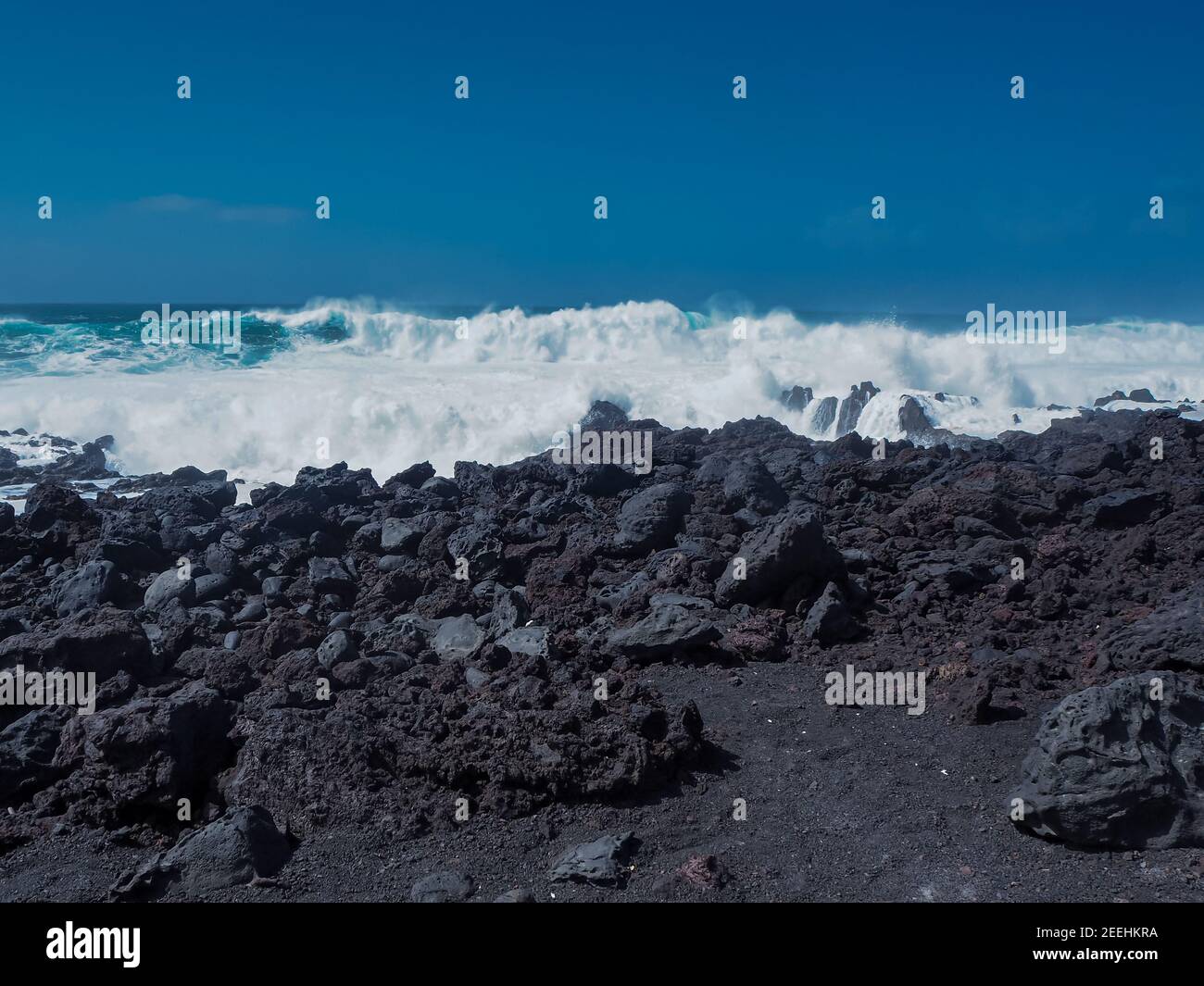 Atlantic waves with white surf meeting the black volcanic coast at El Golfo, Lanzarote, Canary Islands, with a clear blue sky Stock Photo