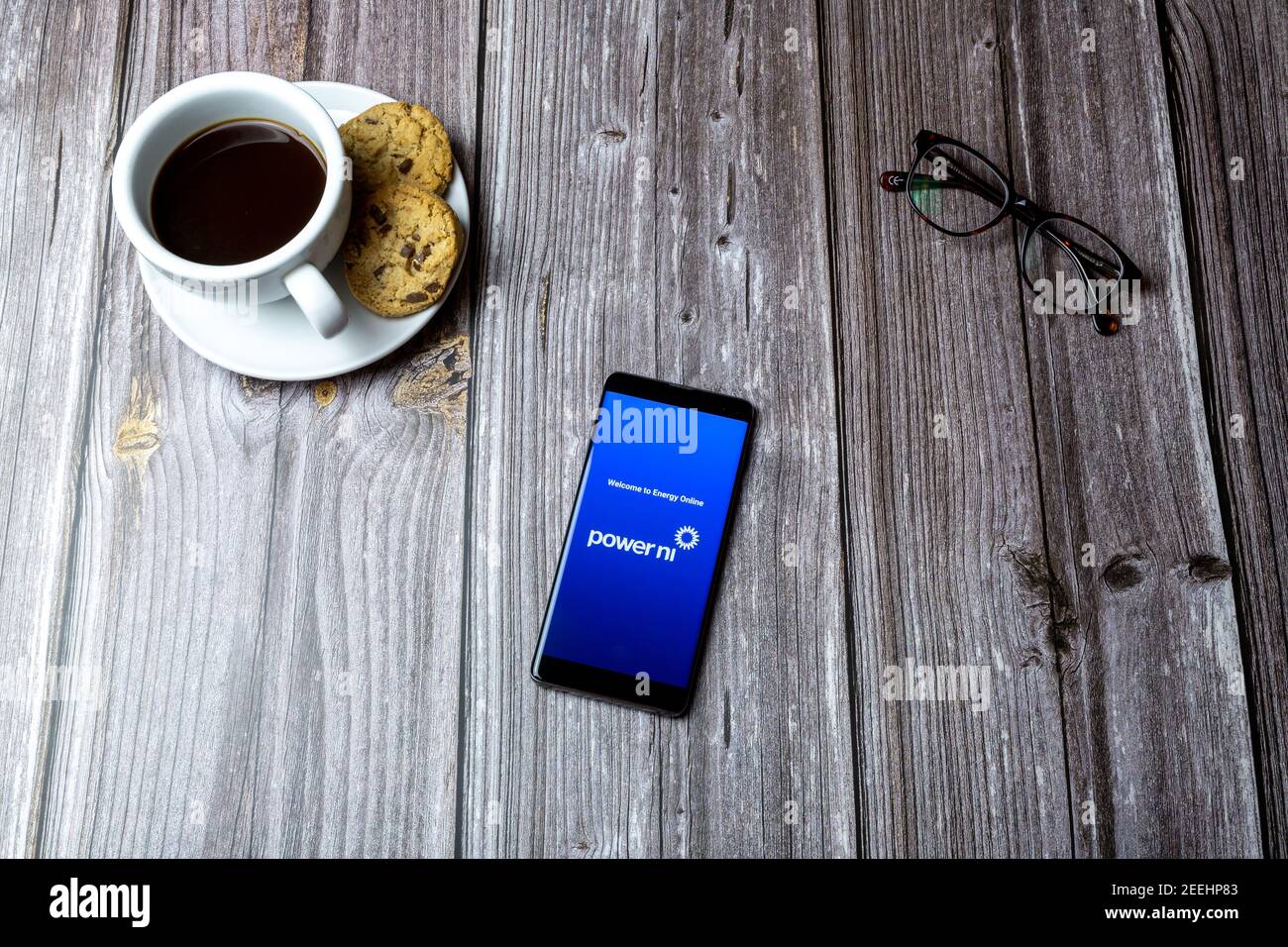 A mobile phone or cell phone laid on a wooden table with the Power NI app open on screen Stock Photo