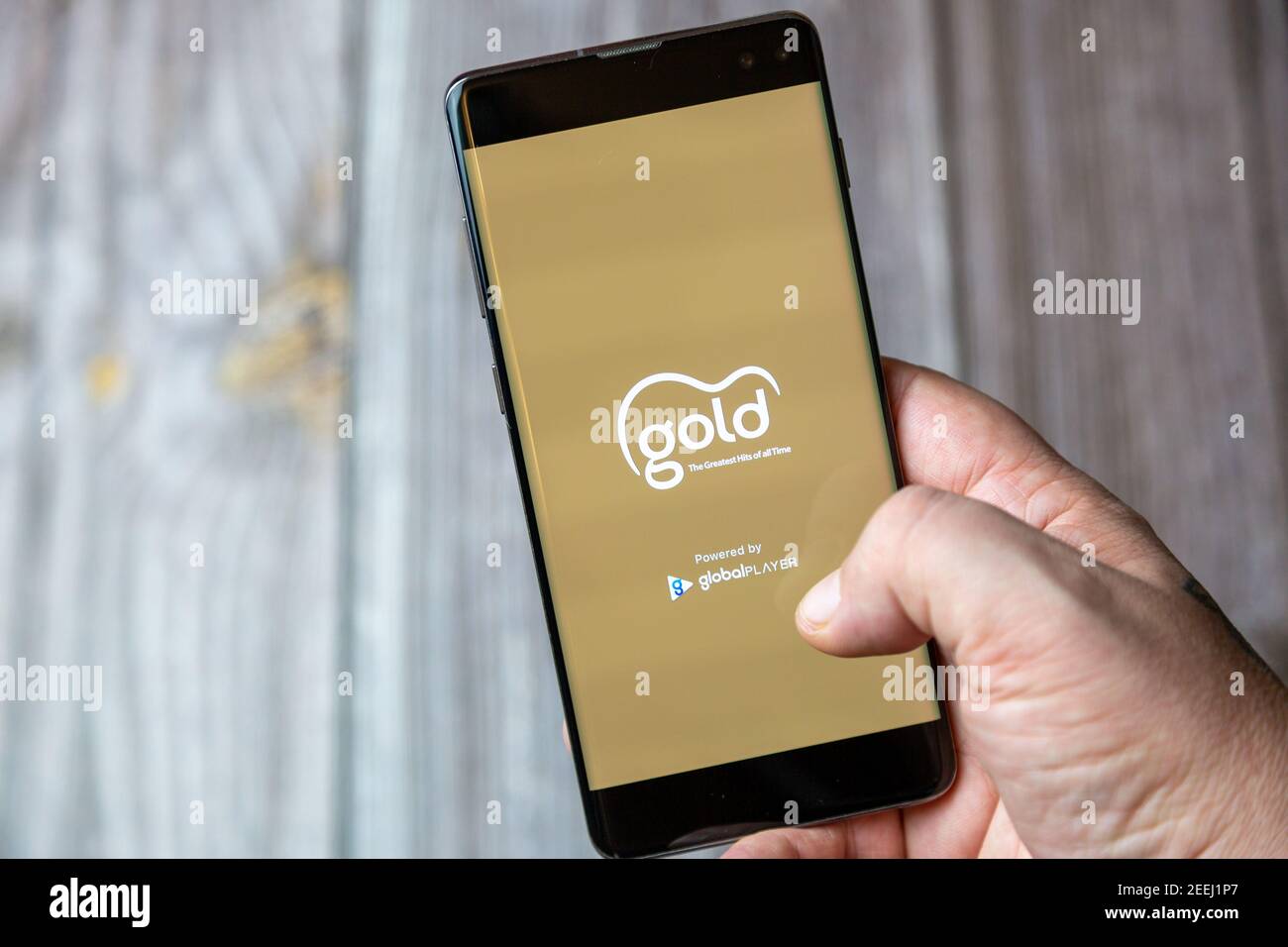 A mobile phone or cell phone being held in a hand with the gold radio app open on screen Stock Photo
