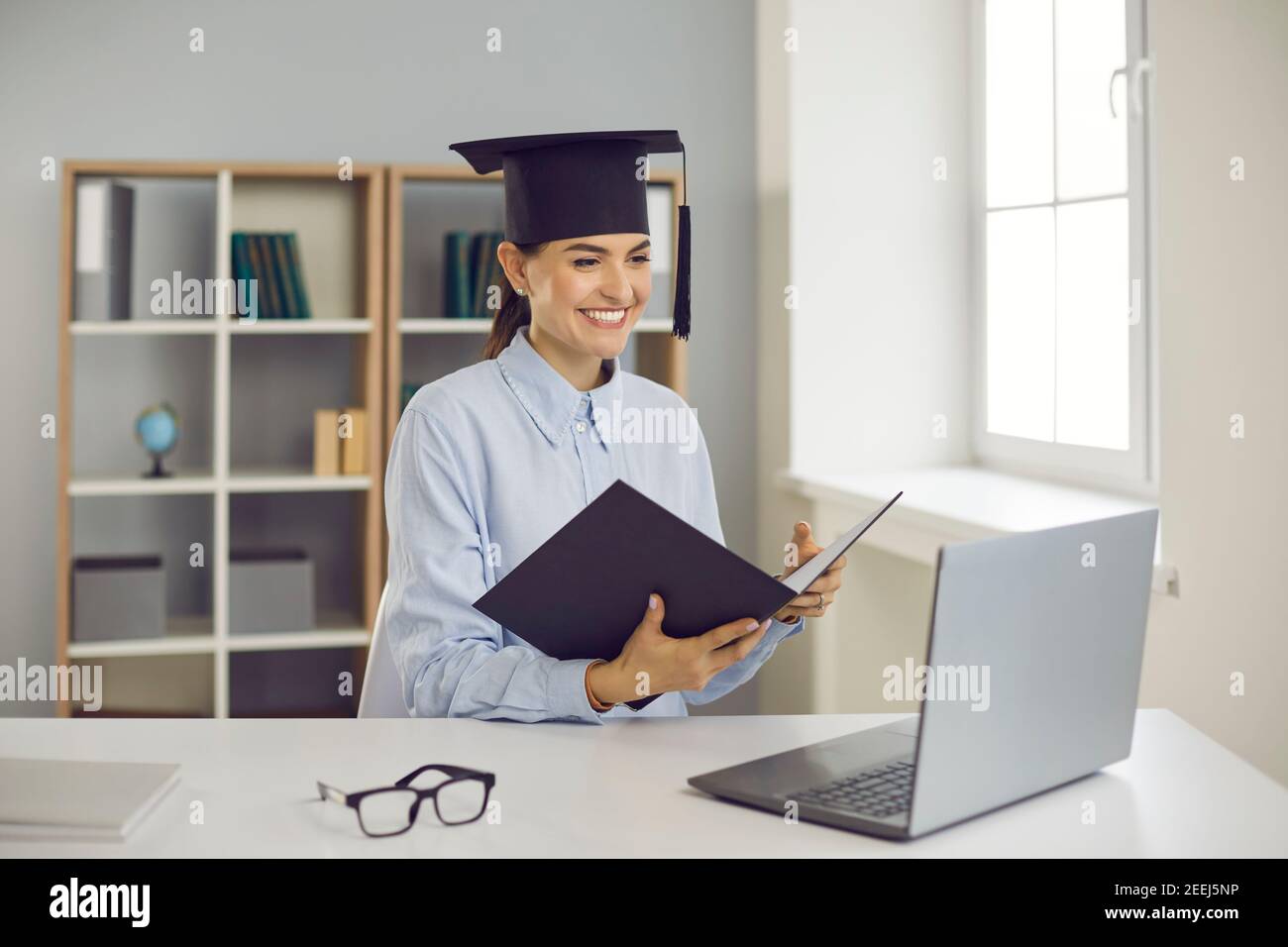 Happy graduate sitting at laptop computer and presenting her thesis remotely via video call Stock Photo