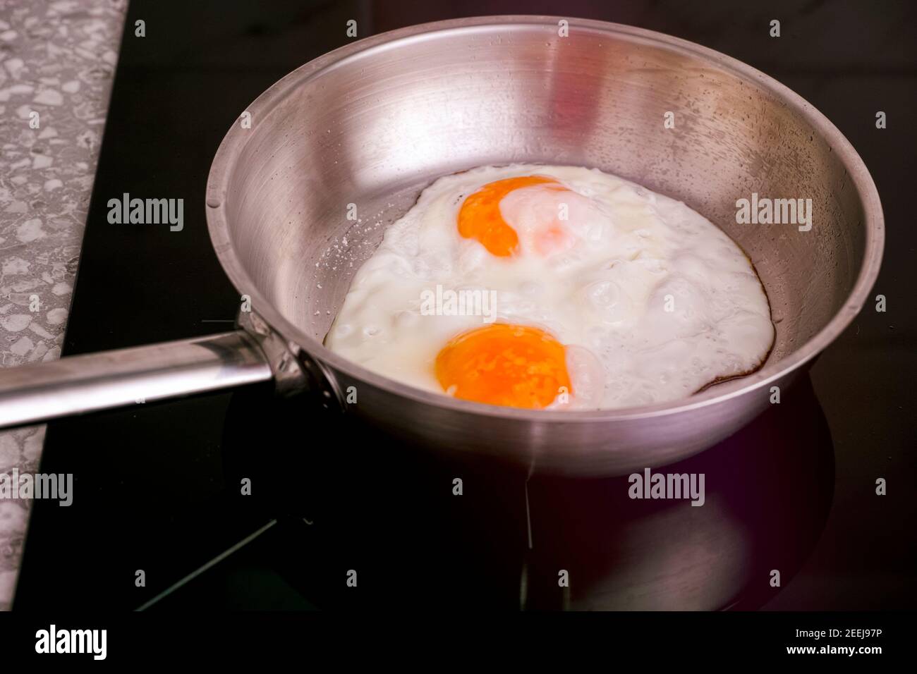 Two eggs in frying pan cooking on induction hob. Closeup Stock Photo