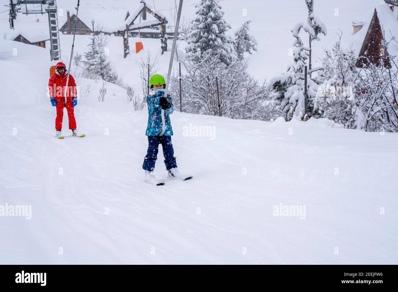 AURON, FRANCE-01.01.2021: Professional ski instructor and child lifting on the ski drag lift rope to the mountain during snowfall. Family and children active vacation concept. Blurred focus background Stock Photo