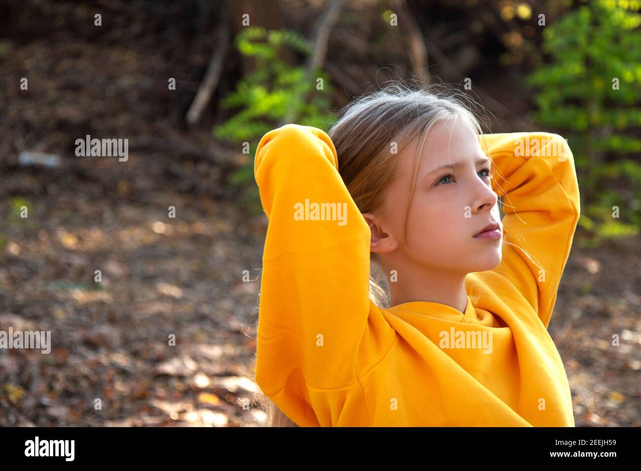 Beautiful teen blonde girl in a bright orange sweatshirt and jeans in an autumn park. Autumn portrait in the forest Stock Photo