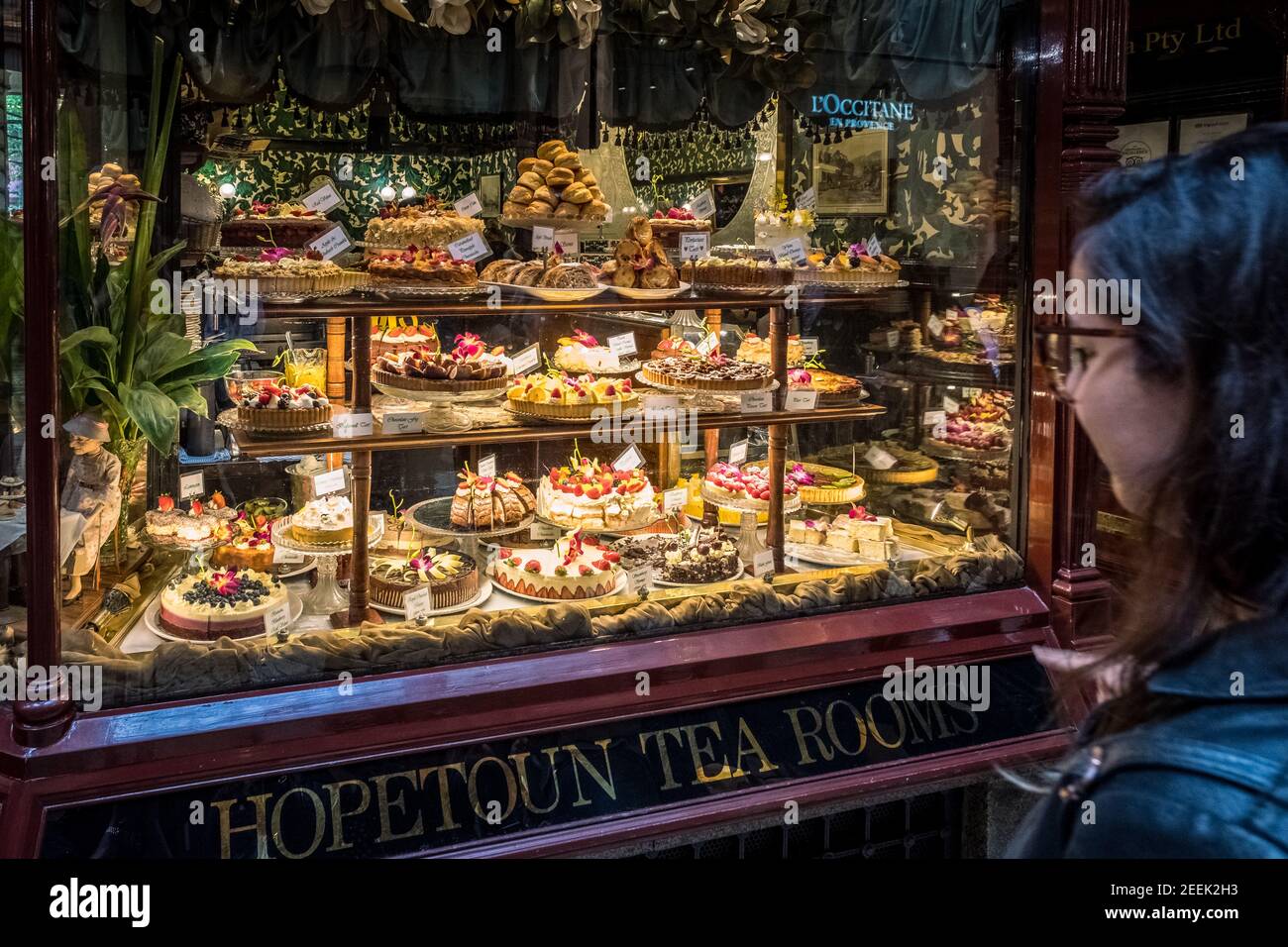 A woman looks at a cake display in the window of the Hopetoun Tea Rooms in Melbourne Stock Photo