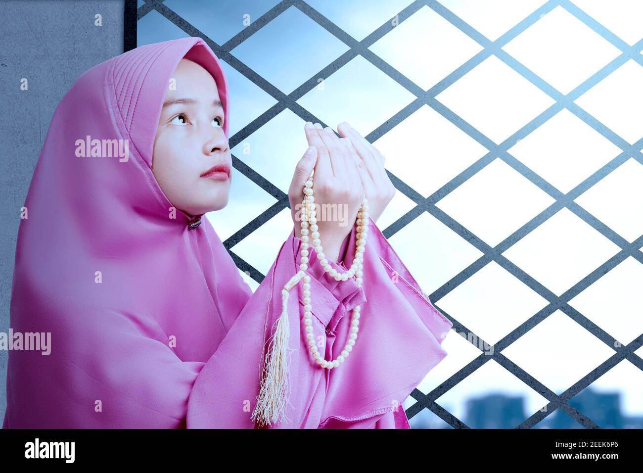 Asian Muslim woman in a veil standing while raised hands and praying on ...