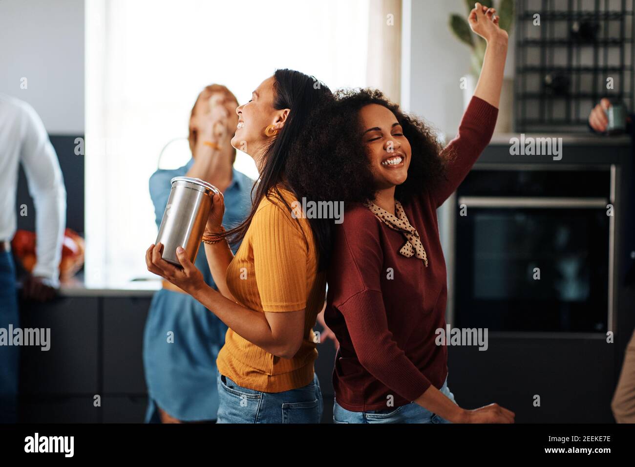 Laughing group of diverse young friends dancing and singing during a party in a friend's kitchen Stock Photo