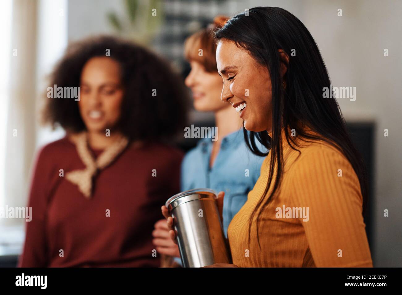 Young woman laughing while hanging out with her diverse group of female friends in an apartment kitchen Stock Photo
