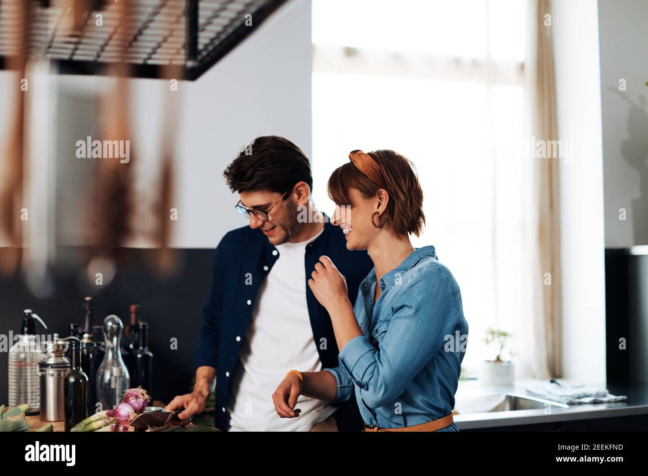 Laughing young couple chopping vegetables at a counter in their kitchen while preparing dinner together Stock Photo