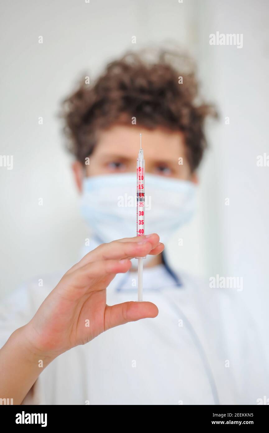 Cute little boy wears a medical uniform and a mask, holds a syringe, playing doctor. Serious child pretending to be a pediatrician Stock Photo
