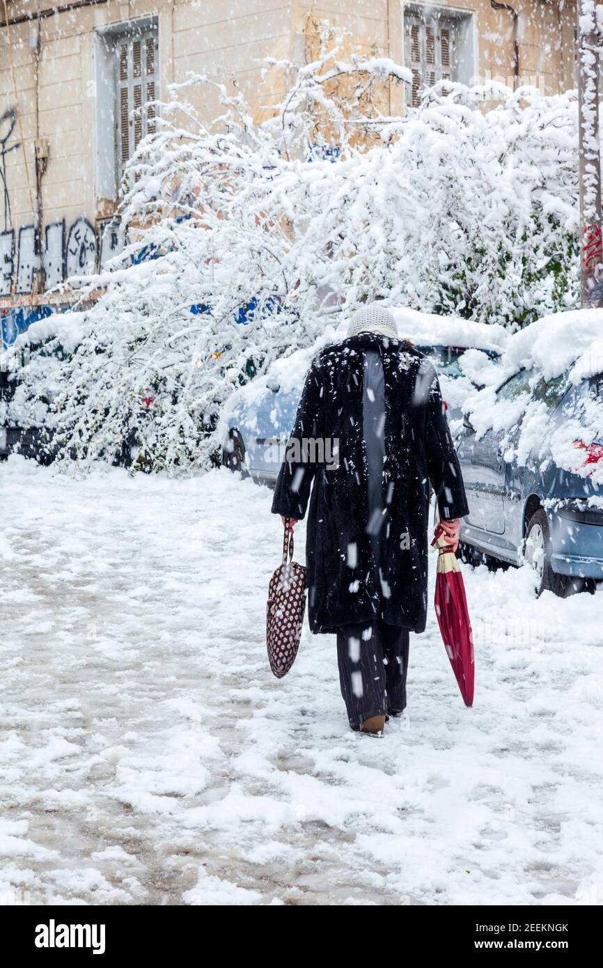 Old lady walking carefully during snowfall in Athens city, capital of Greece, Europe Stock Photo