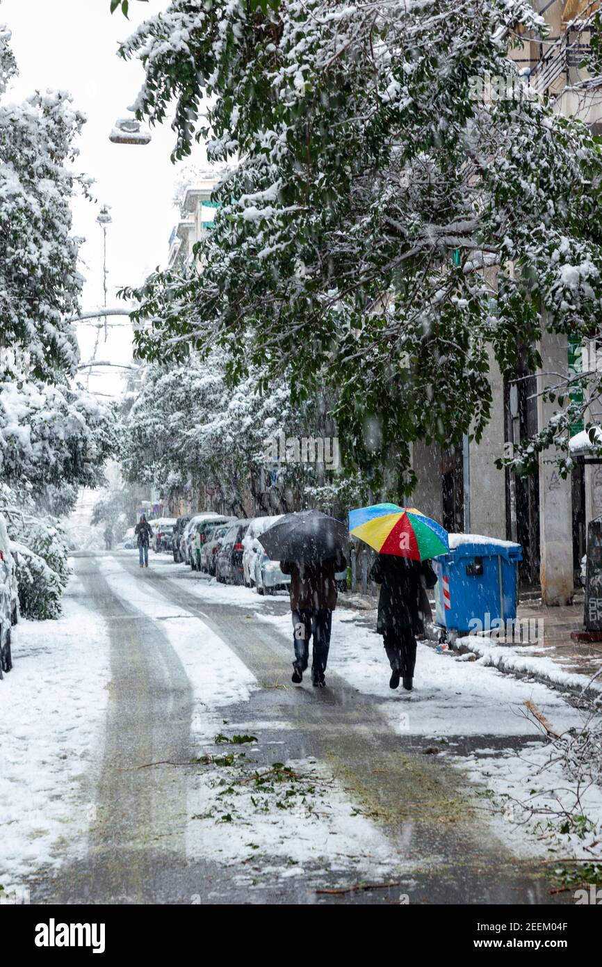 Couple walking down the street holding colorful umbrella during snowstorm in Athens city, capital of Greece, Europe Stock Photo
