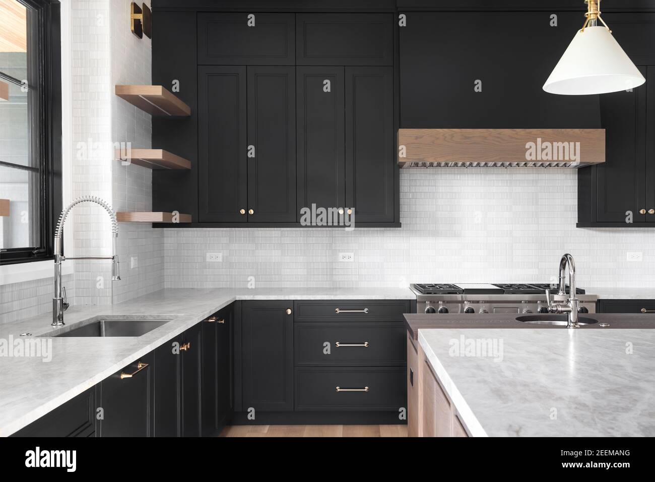 A luxury kitchen with black cabinets, granite counter top, tiled backsplash, stainless steel appliances, and chrome faucets. Stock Photo