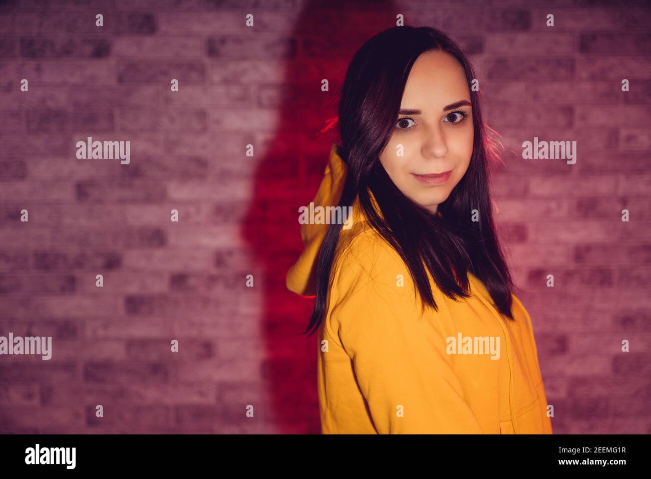 A young woman in a fashionable yellow hoodie. Portrait of a beautiful woman in a yellow hoodie against background of brick wall. Stock Photo