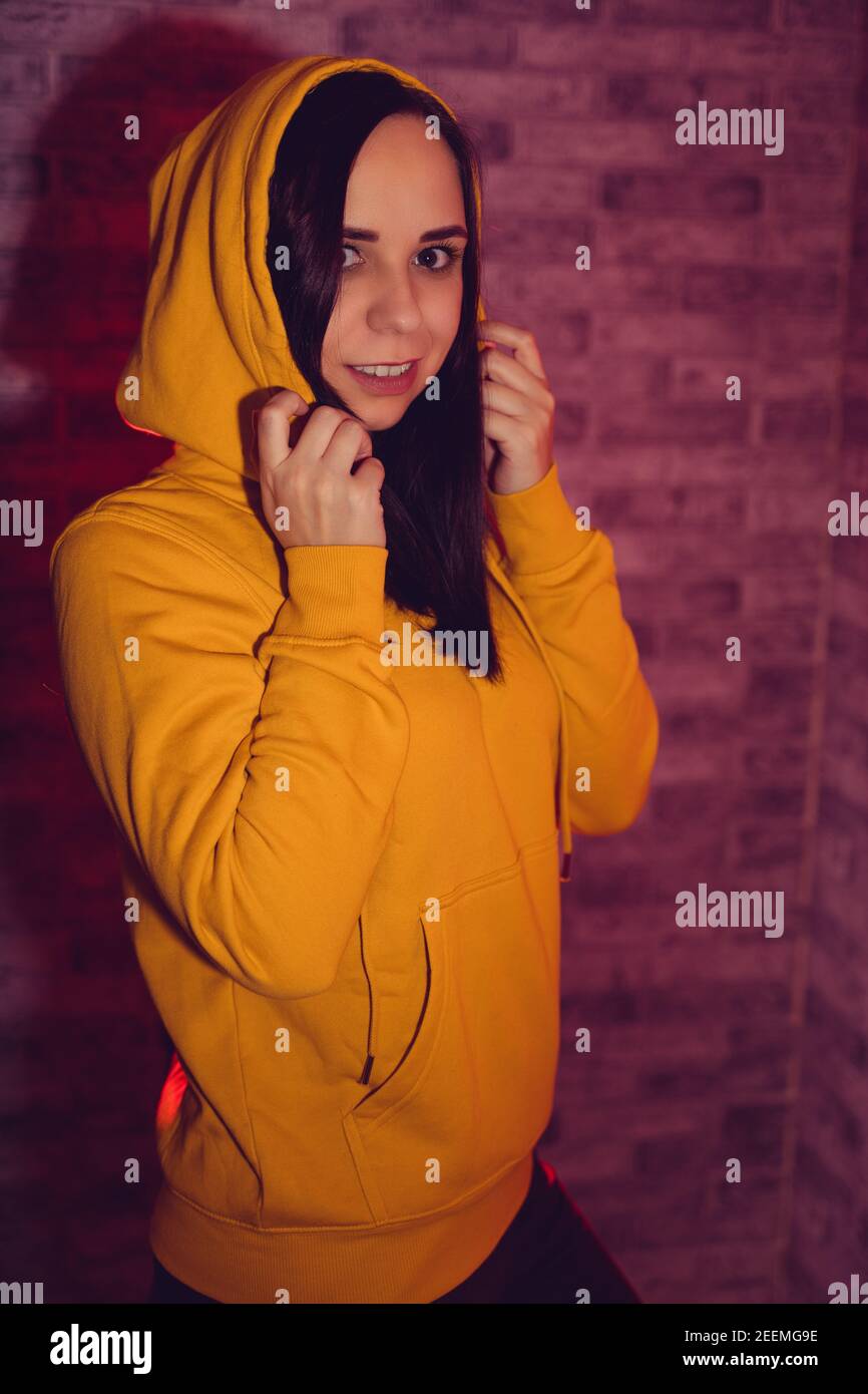 A young woman in a fashionable yellow hoodie. Portrait of a beautiful woman in a yellow hoodie against background of brick wall. Stock Photo