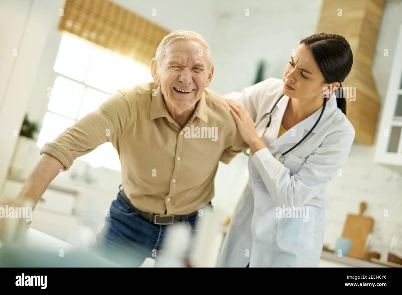 Concerned female doctor furrowing her brow while helping senior man to get up from the chair Stock Photo