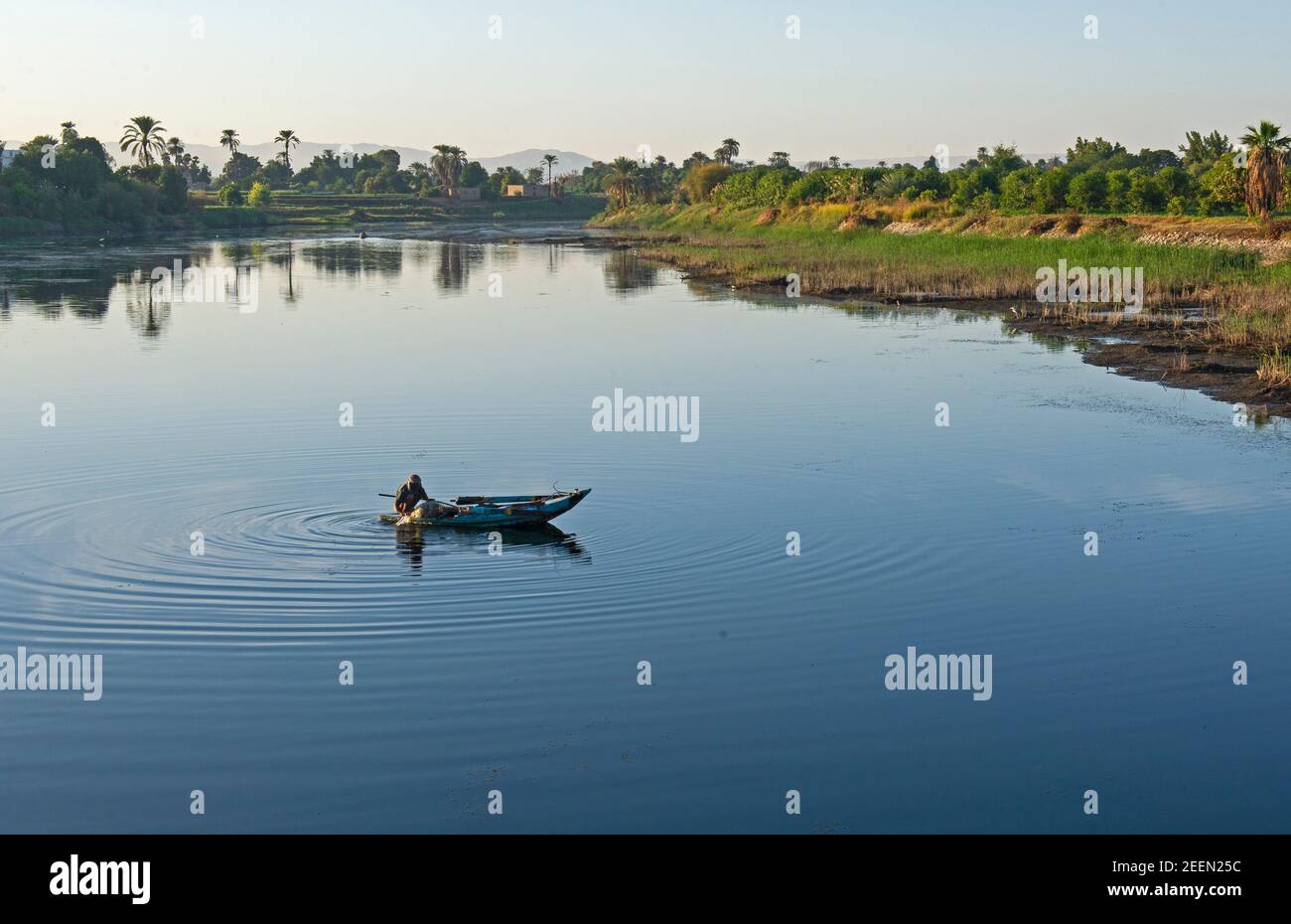 Traditional egyptian bedouin fisherman in rowing boat on river Nile fishing by riverbank Stock Photo
