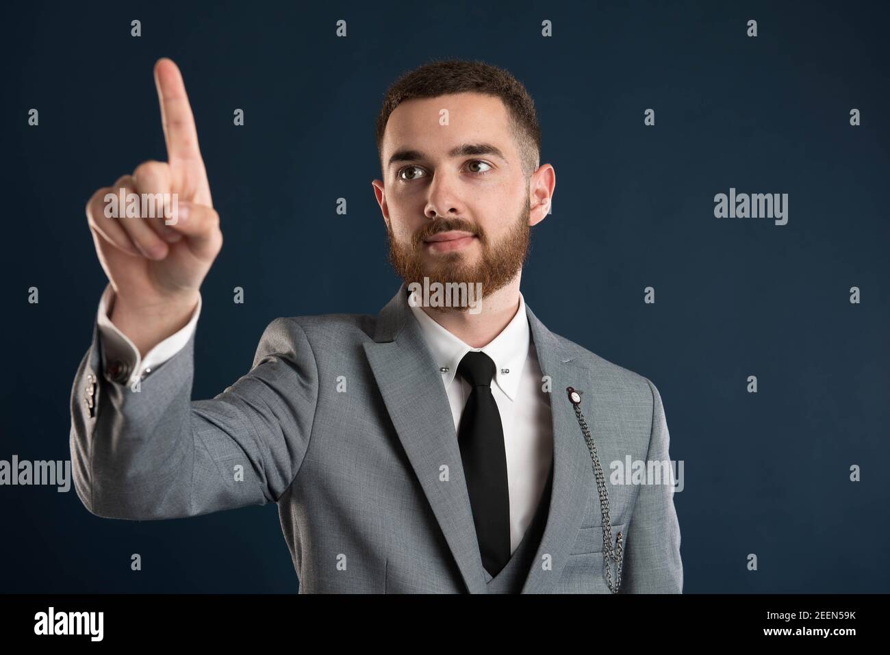 Smiling young businessman pointing at a virtual screen wearing a grey suit and black tie Stock Photo