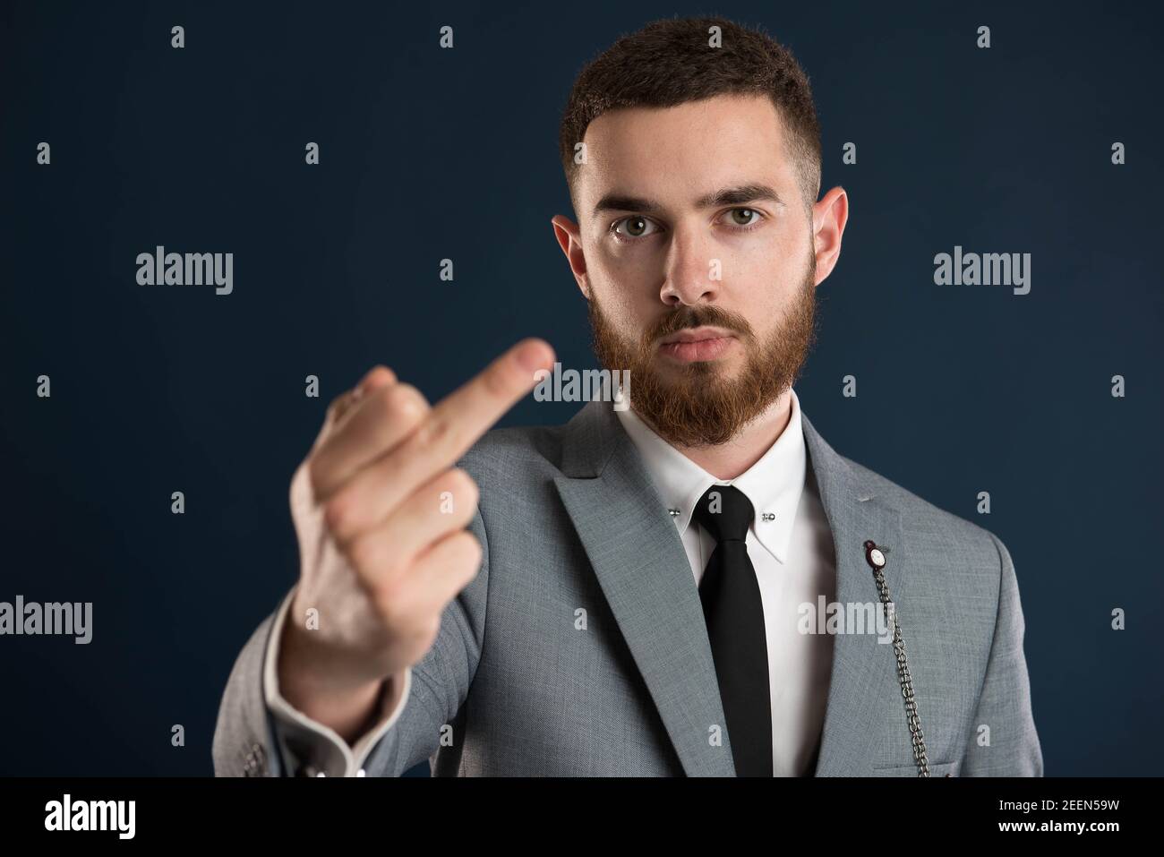 Serious young businessman showing obscene sign wearing a grey suit and a black tie Stock Photo