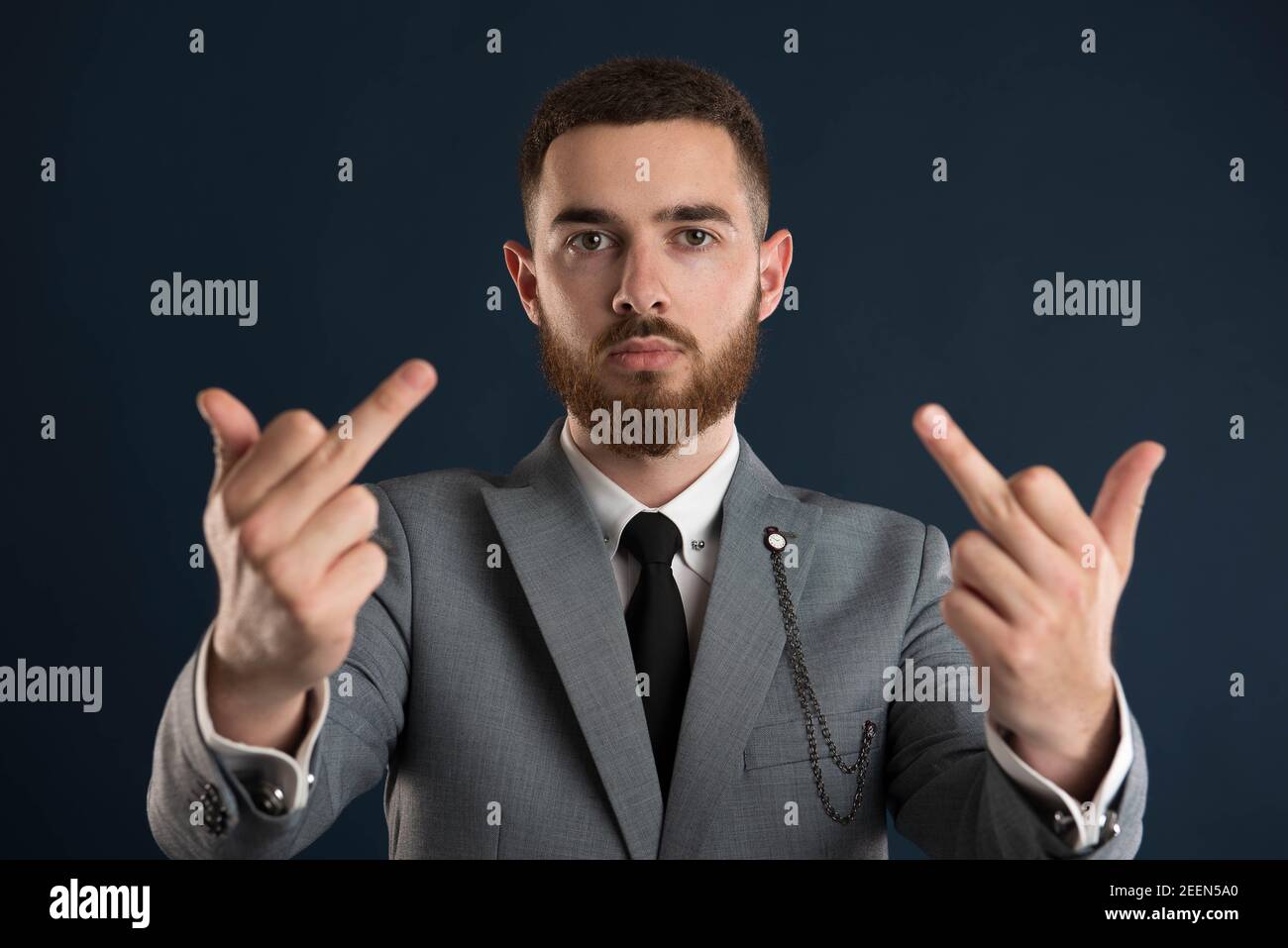 Serious young businessman showing double fuck you wearing a grey suit and a black tie Stock Photo
