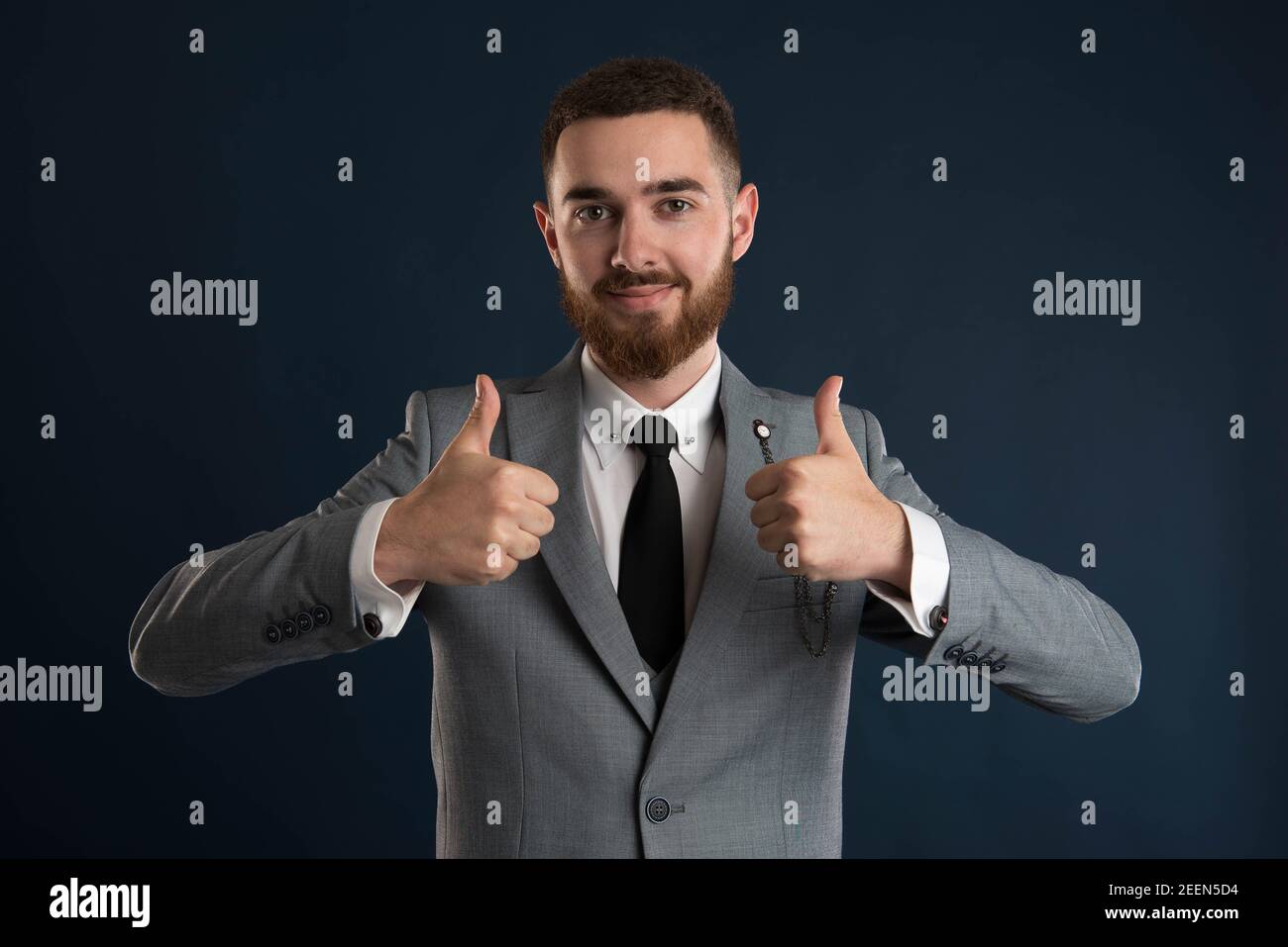 Smiling businessman showing double thumbs up wearing a black tie and grey suit Stock Photo