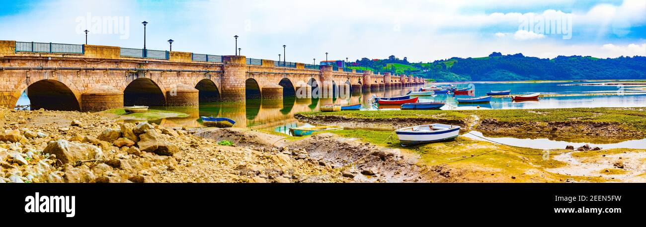 Scenic mountain and sea panoramic landscape in northern Spain.Green meadows and boats under the medieval stone bridge Stock Photo