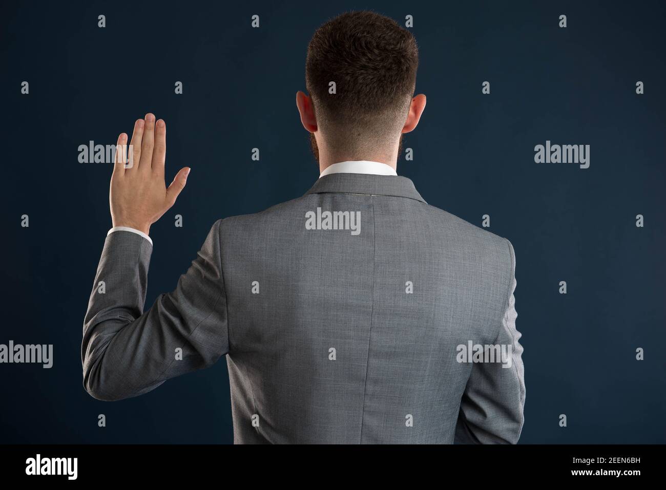 Young businessman taking an oath with his back to the camera wearing a grey jacket Stock Photo
